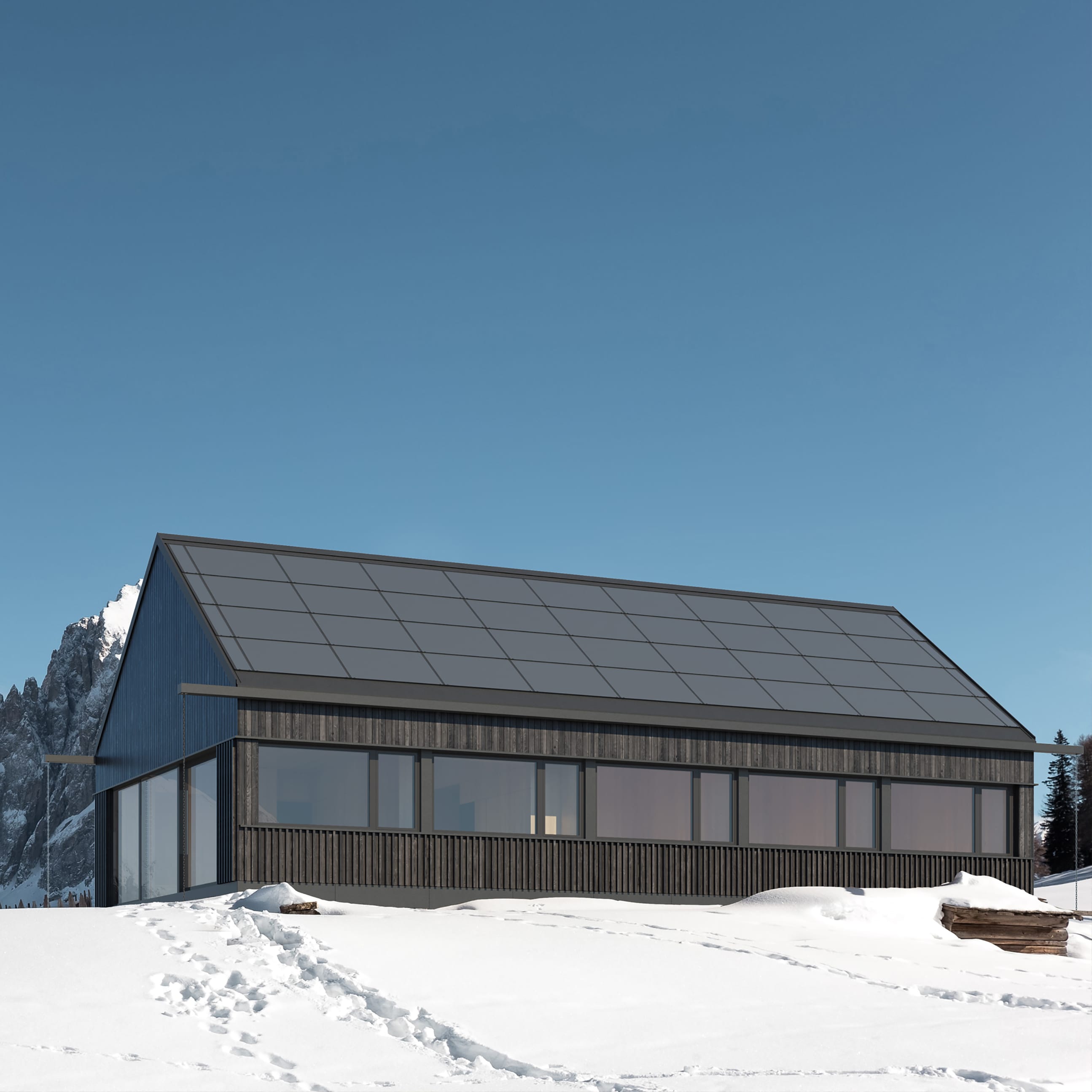 A long, modern building with a dark wood facade and a roof covered with solar panels. The house stands on a snowy mountain slope.