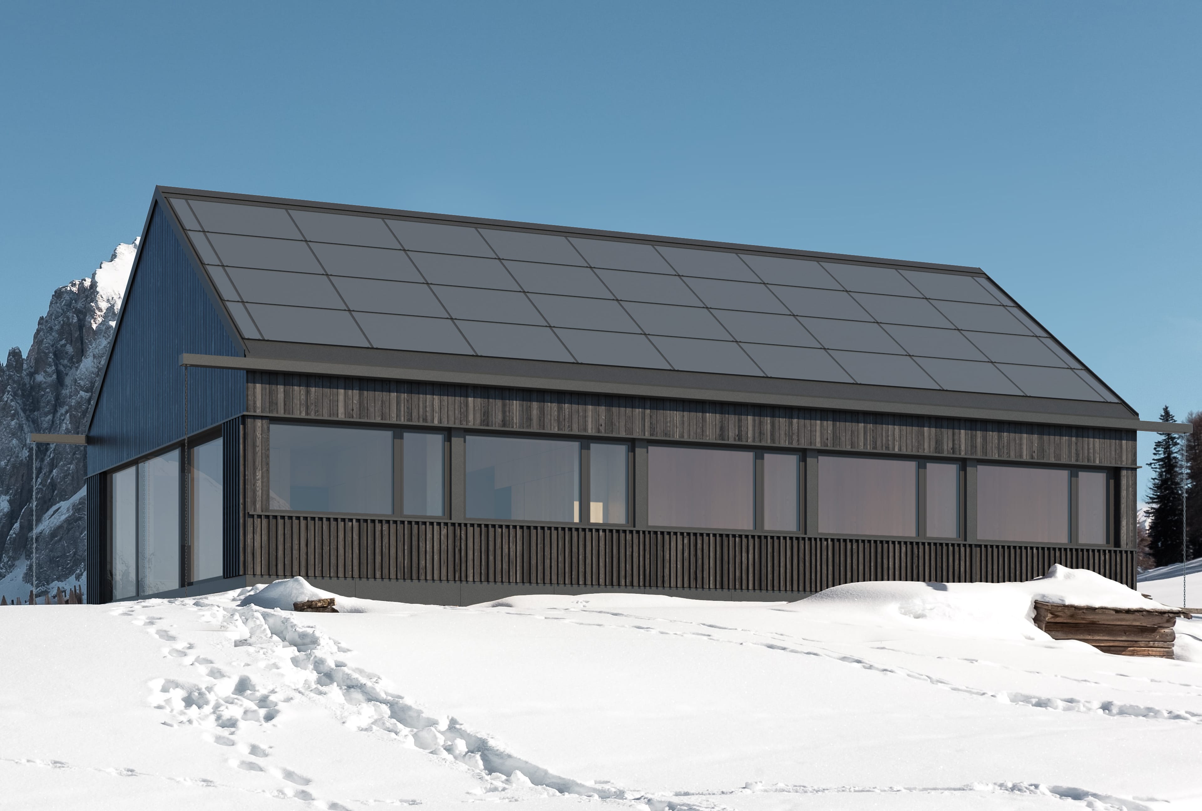 A long, modern building with a dark wood facade and a roof covered with solar panels. The house stands on a snowy mountain slope.