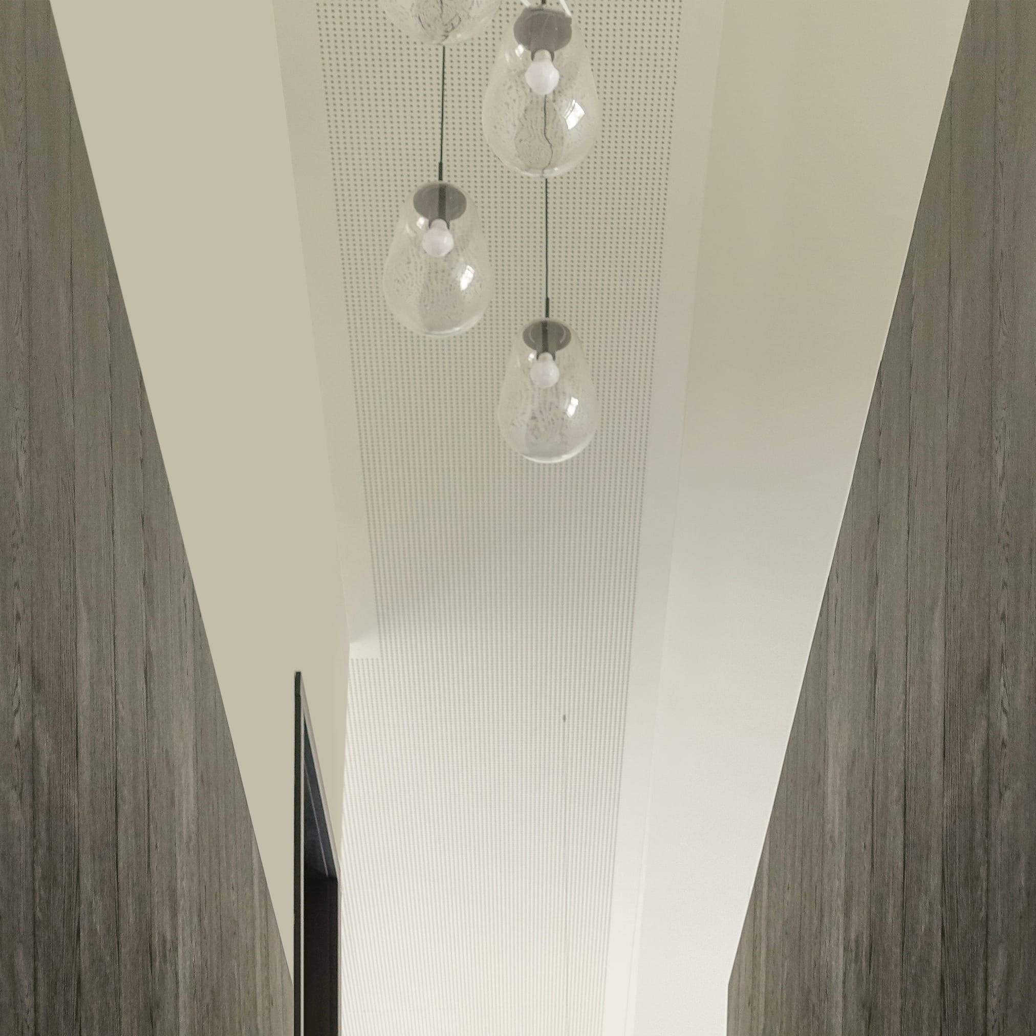 Nowoczesne, szklane lampy wiszące o organicznym kształcie, zwisające z białego, perforowanego sufitu.