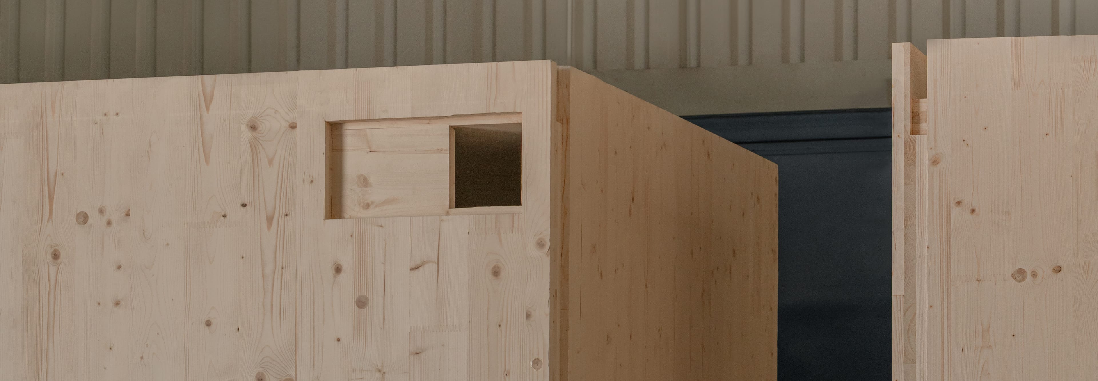 A close-up of massive, prefabricated modules of light structural wood (CLT) standing in a production hall.