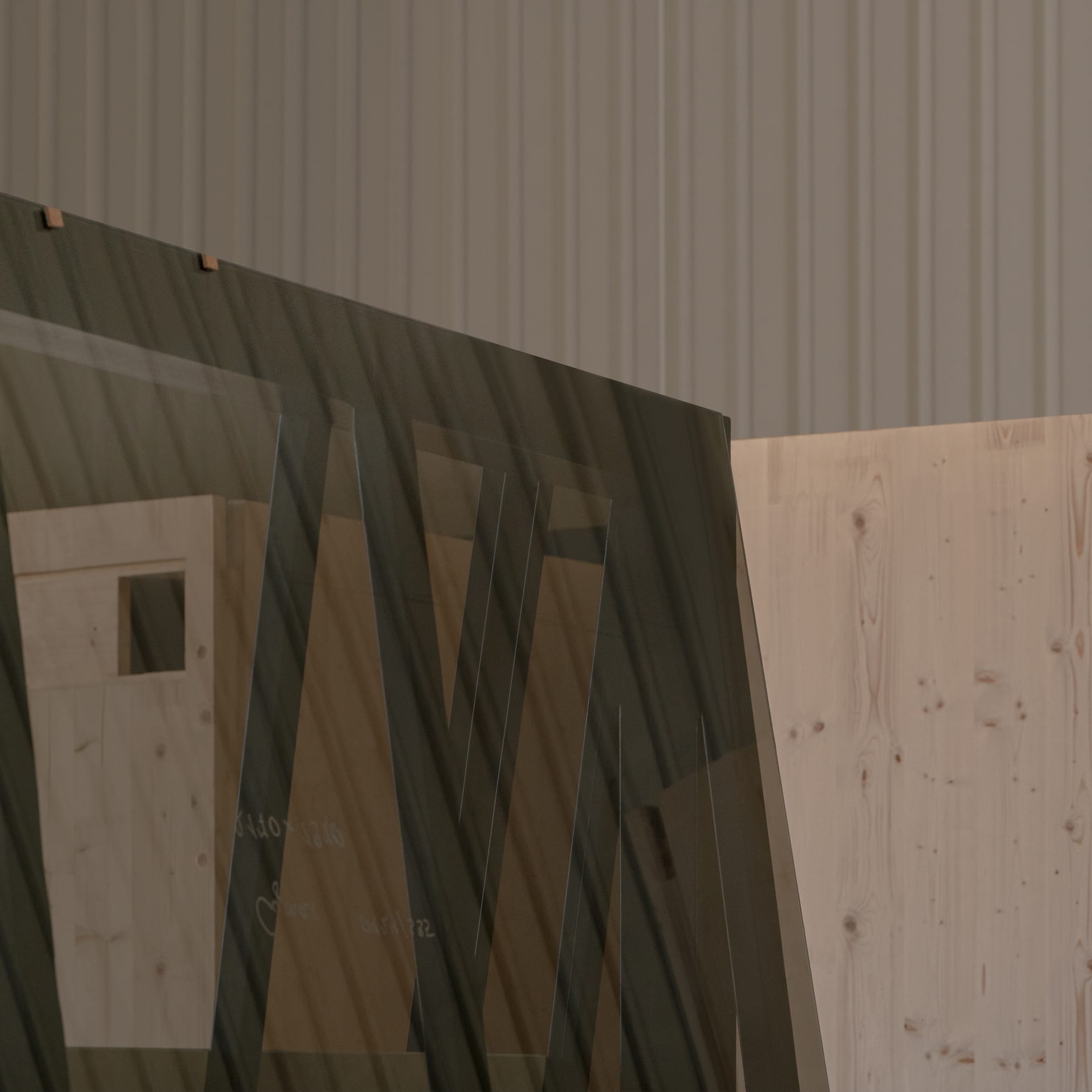 Large sheets of glass stand against a wall of light-colored construction wood in a hall. Above, a wall of corrugated iron is visible.
