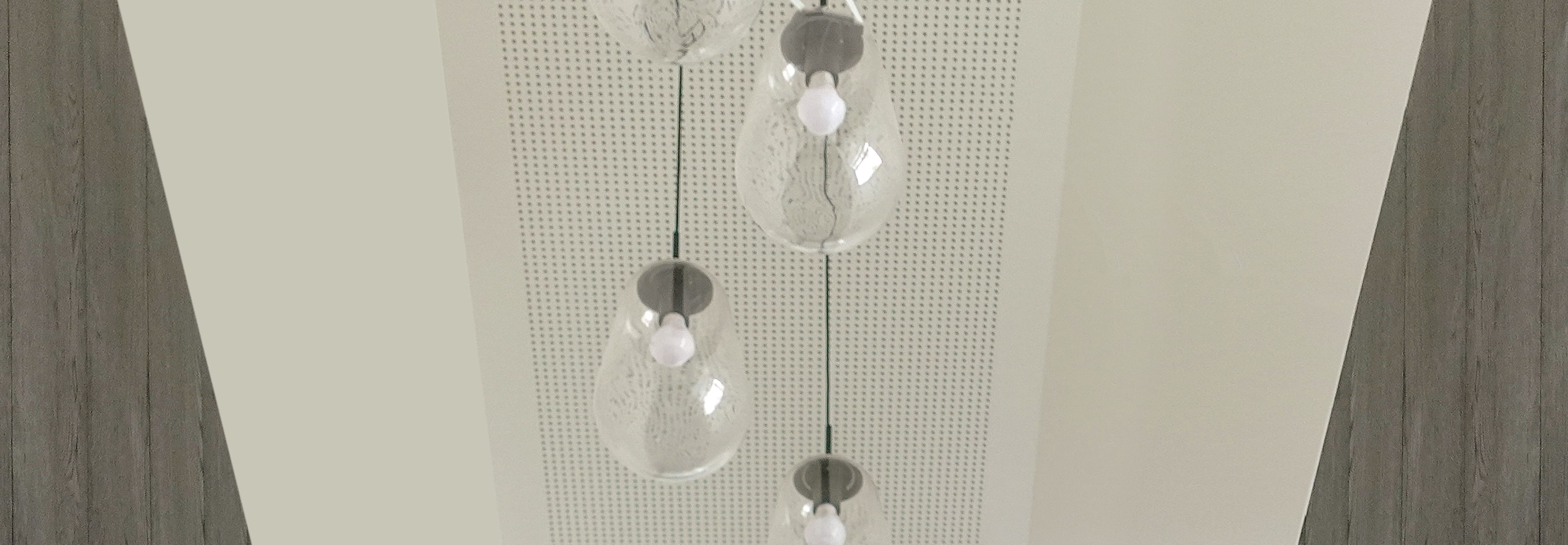 Modern, organic-shaped glass pendant lamps hanging from a white, perforated ceiling.