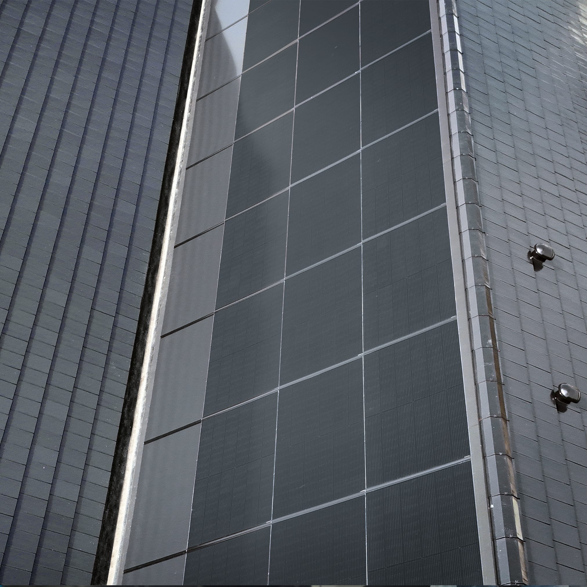 Zbliżenie na połacie dachu, pokazujące połączenie ciemnych, gładkich paneli fotowoltaicznych z teksturowanymi, szarymi dachówkami.