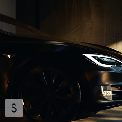 A close-up of the headlight and bumper of a black, luxury electric car in a dark garage.