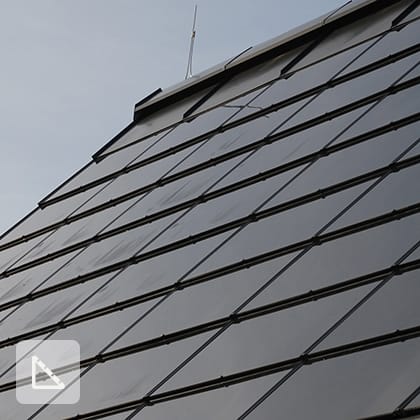 A close-up of a pitched roof covered with dark, integrated photovoltaic panels that form a smooth, uniform surface.