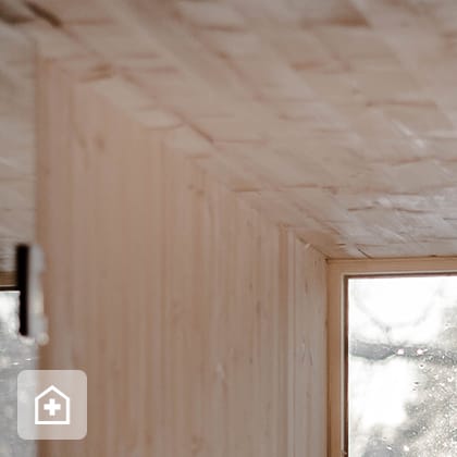 A shot of the interior of a room finished in light wood, showing a corner and a large window with a view of a snowy landscape.