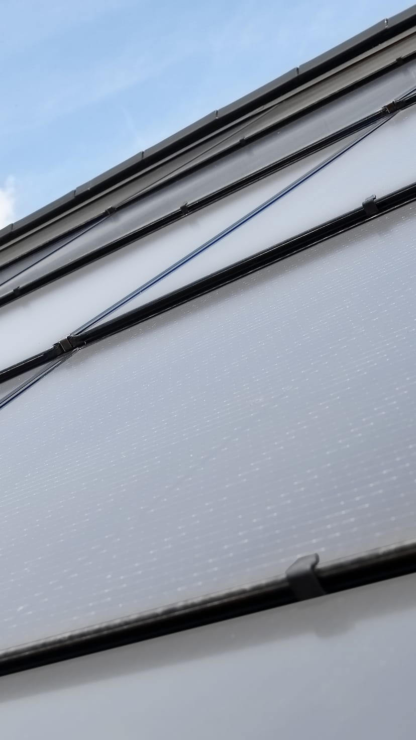 A close-up of a roof slope made of integrated photovoltaic panels in a brick-red color.