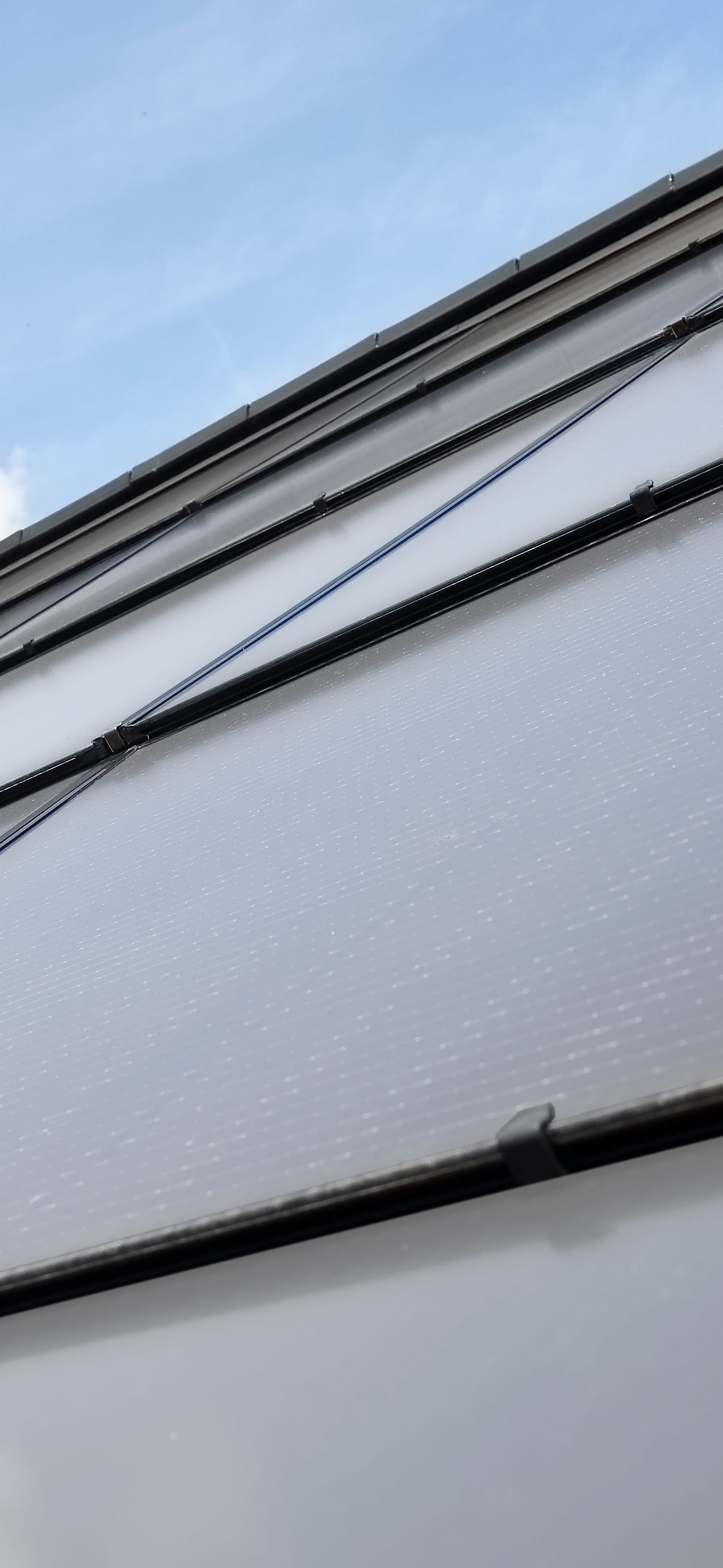 A close-up of a roof slope made of integrated photovoltaic panels in a brick-red color.