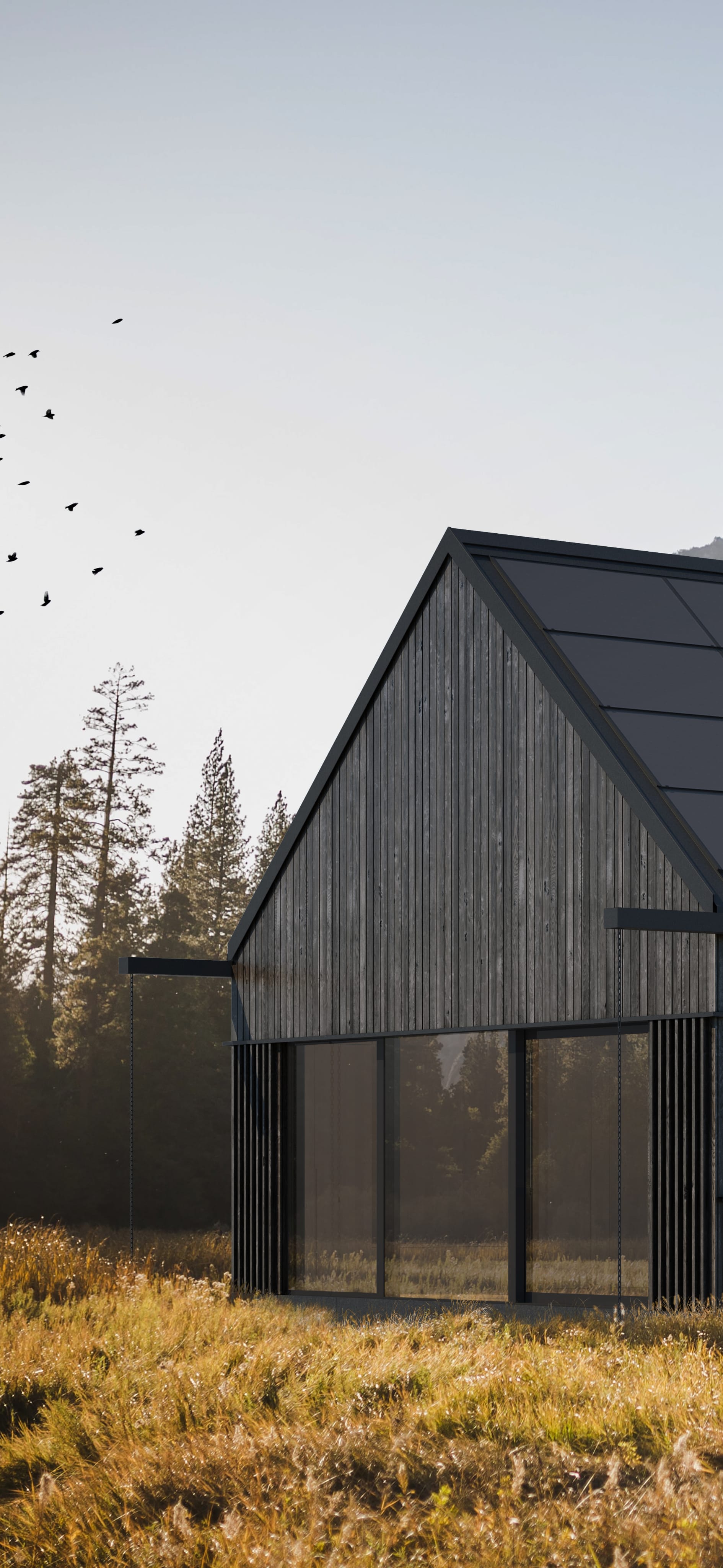 Nowoczesny dom z dachem solarnym i ciemną, drewnianą elewacją stoi na suchej łące u podnóża zalesionych gór.