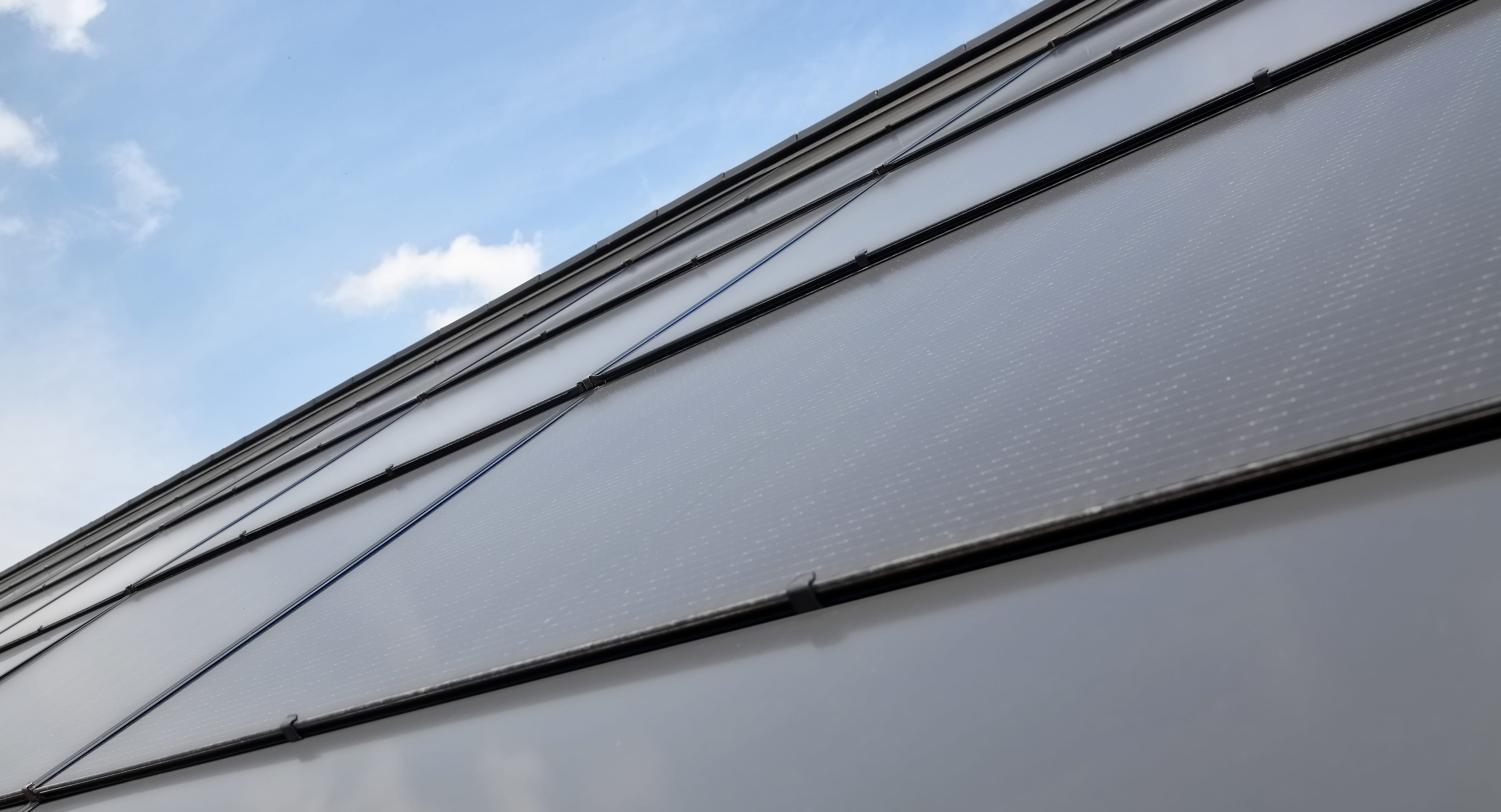 A close-up of a roof slope made of integrated photovoltaic panels in a brick-red color.