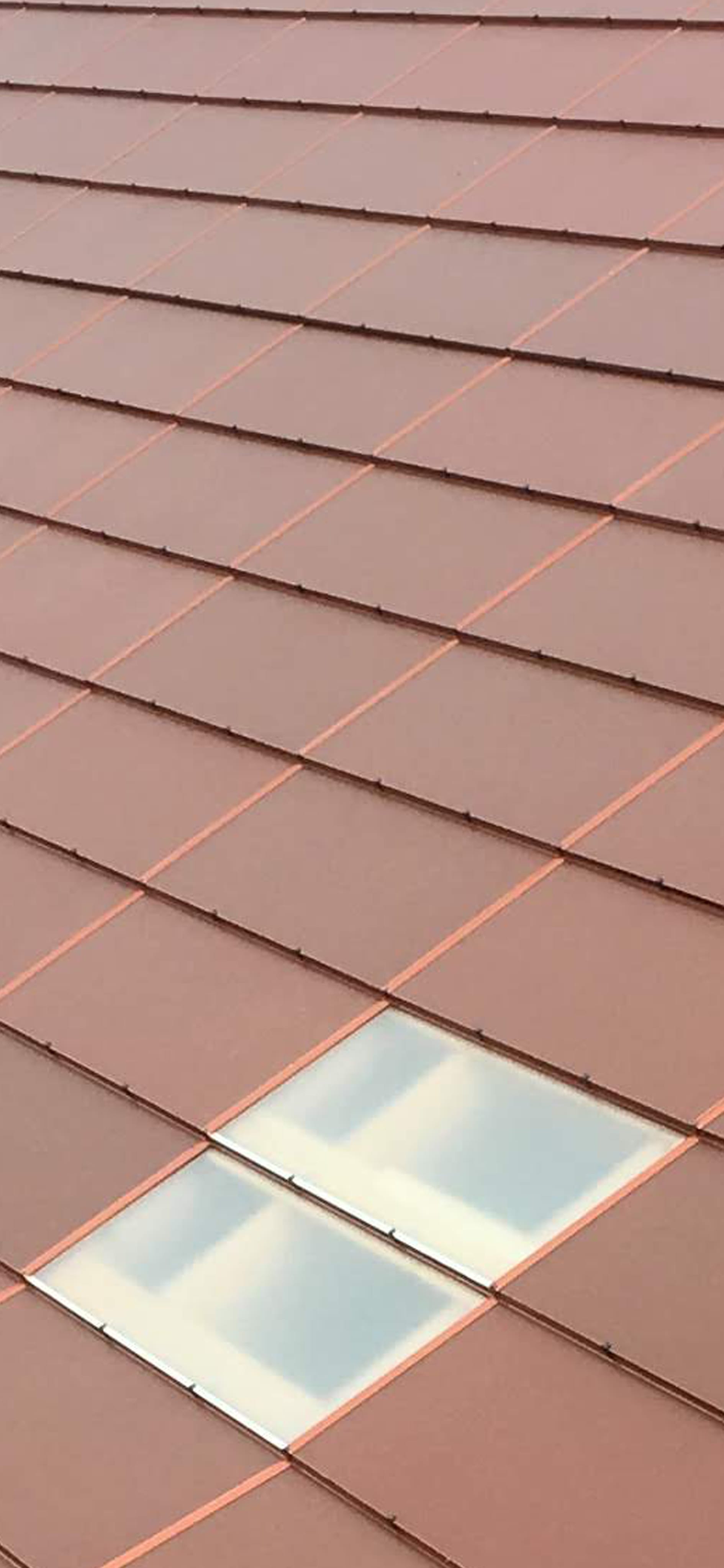 Zbliżenie na połać dachu wykonaną ze zintegrowanych paneli fotowoltaicznych w ceglastym kolorze.