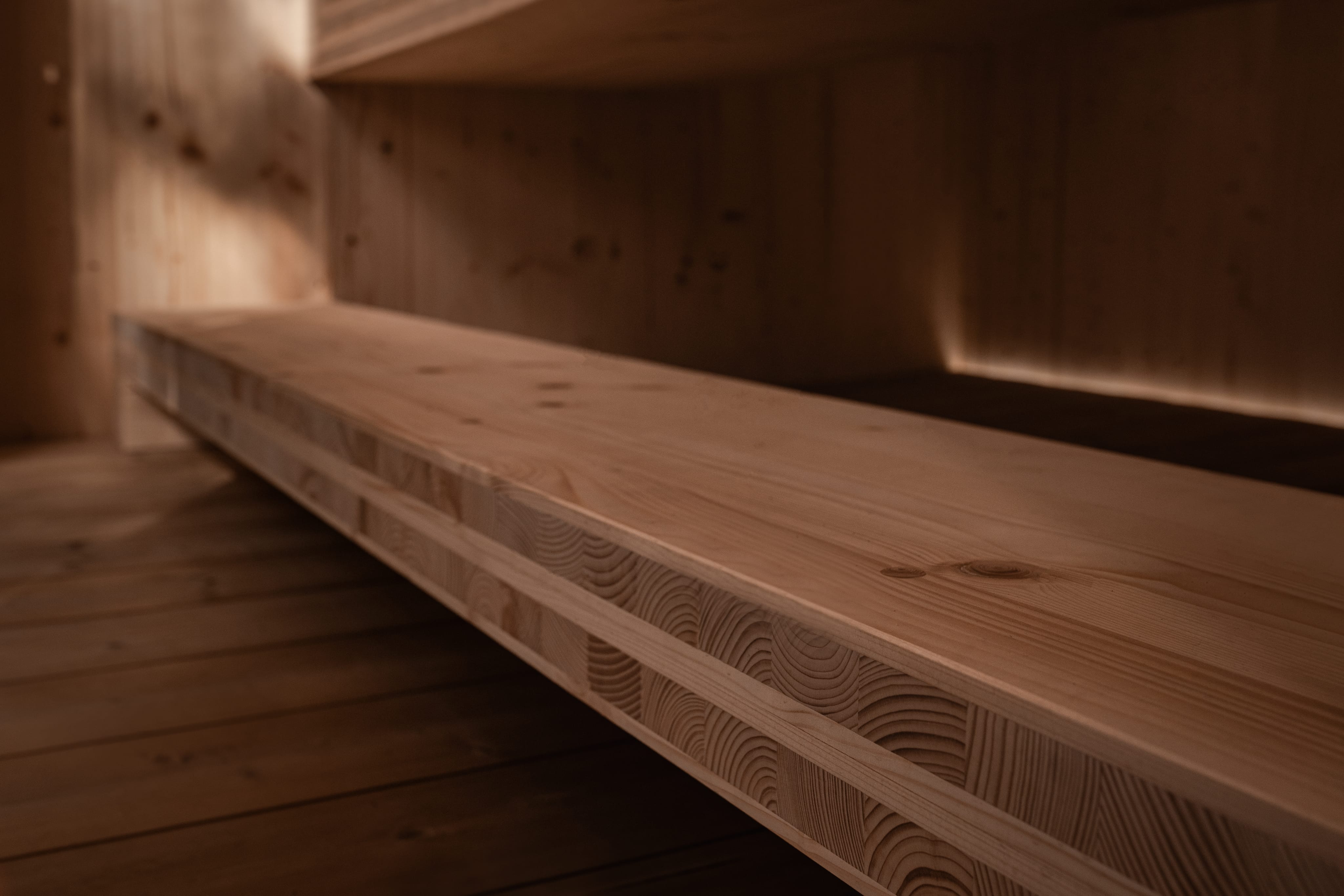An angular close-up of a solid light wood beam in a sauna, showing its layered construction of glued beams and visible grain.