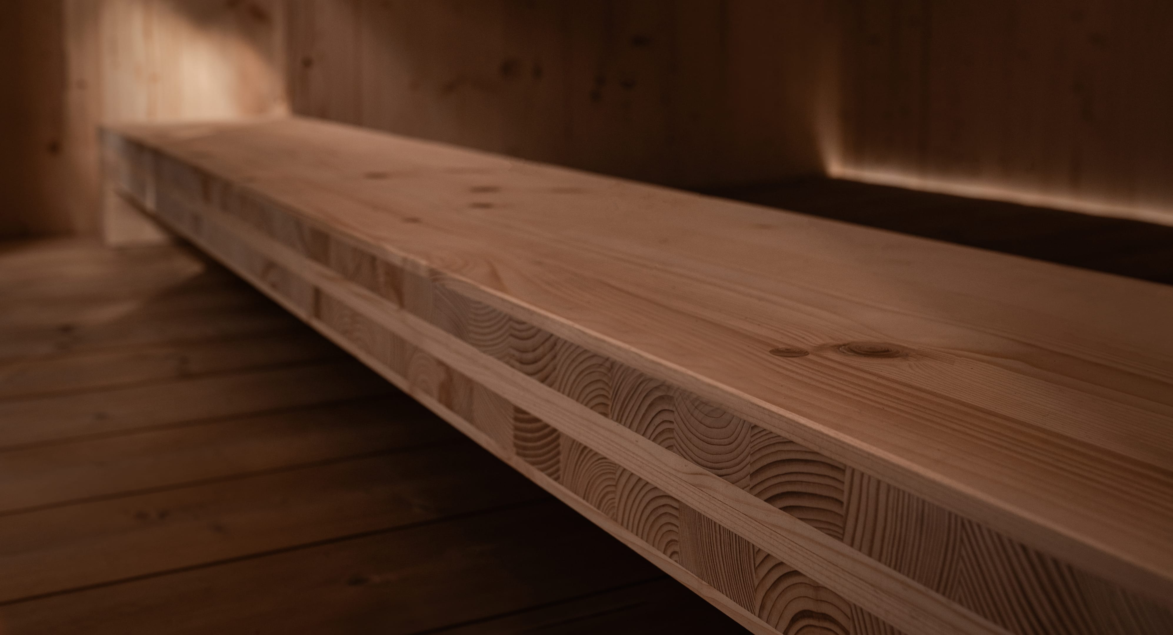 An angular close-up of a solid light wood beam in a sauna, showing its layered construction of glued beams and visible grain.