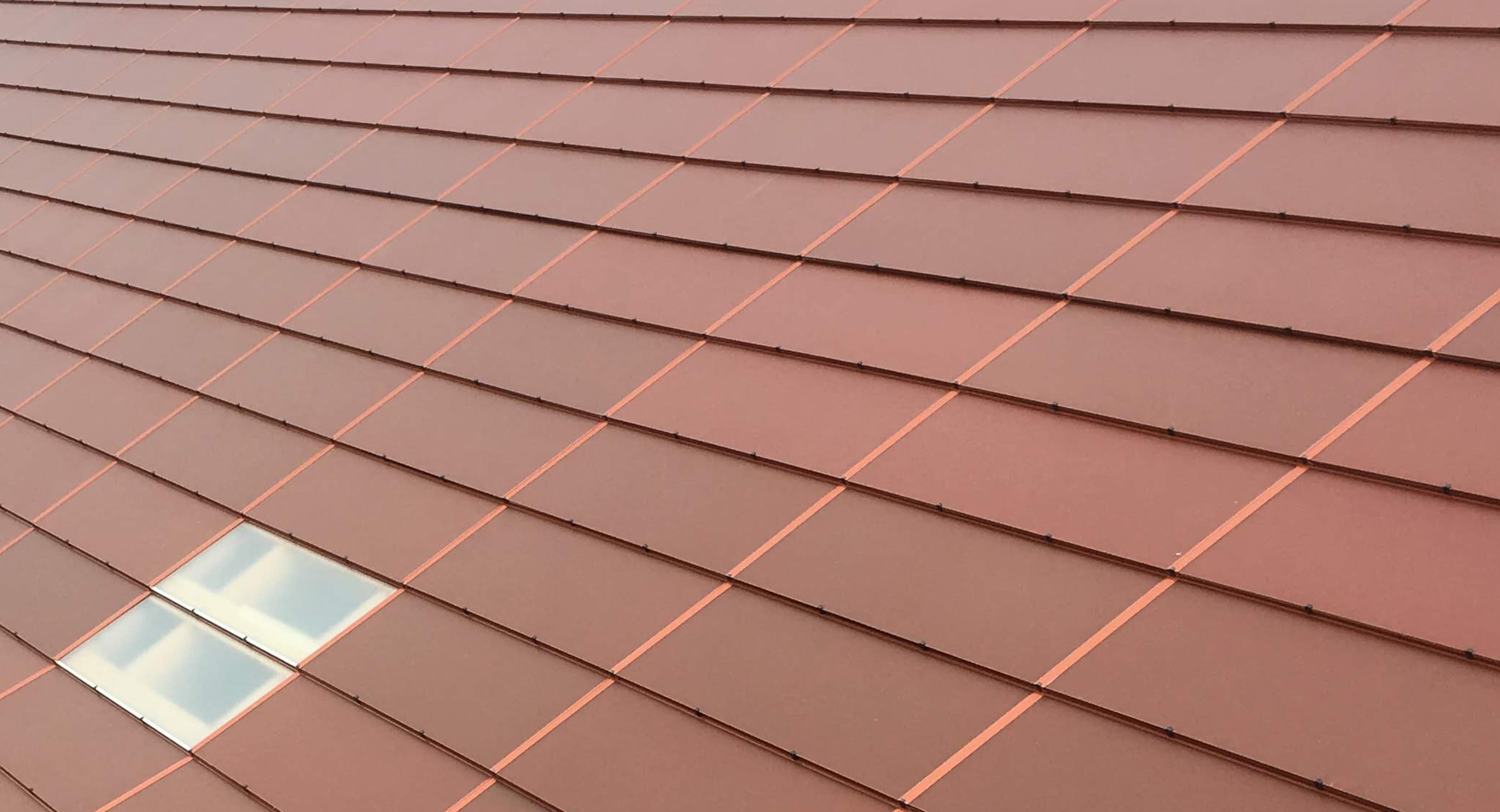 Zbliżenie na połać dachu wykonaną ze zintegrowanych paneli fotowoltaicznych w ceglastym kolorze.