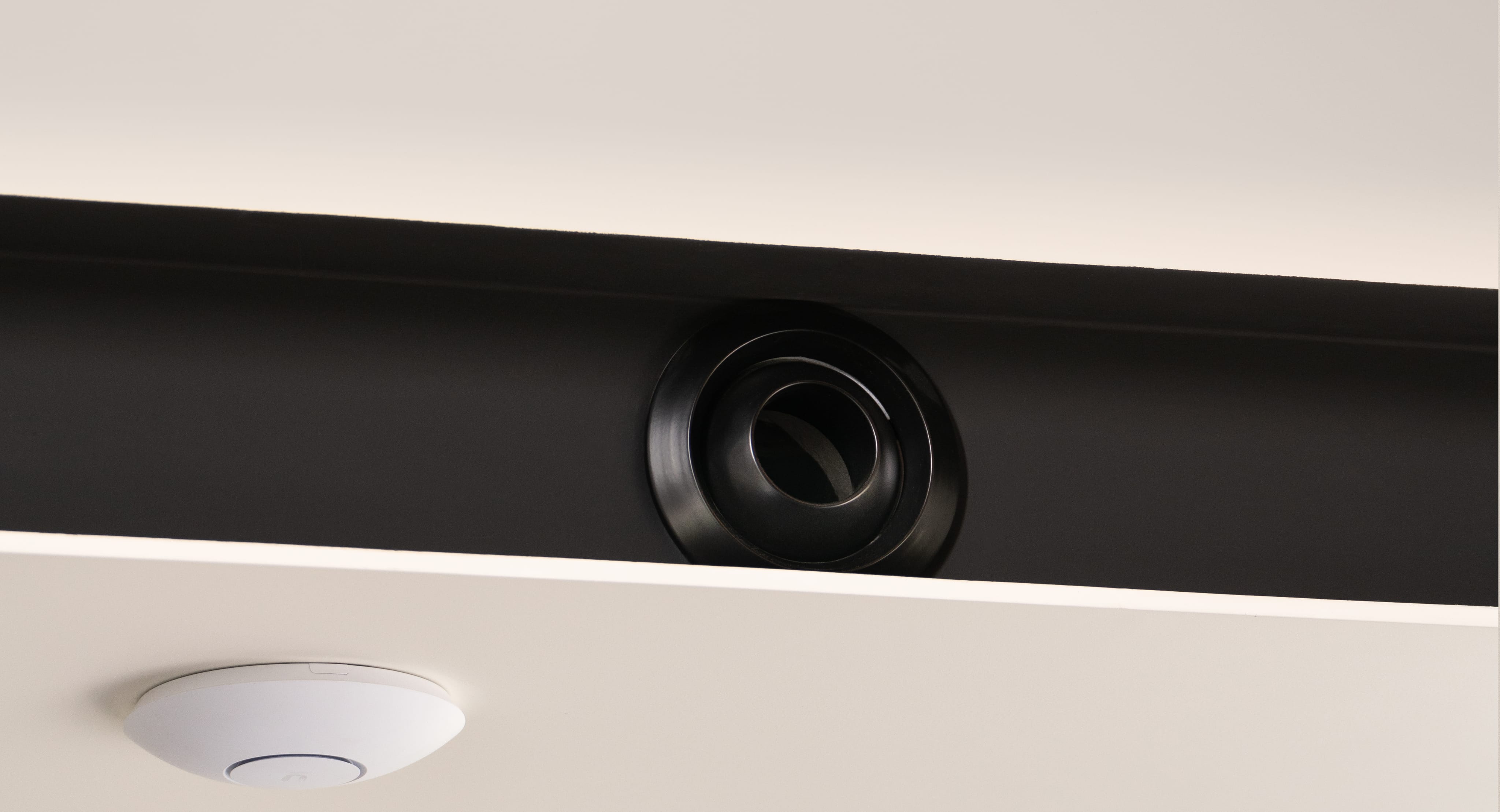 Corner of a bright room with a black ventilation grille on a white wall.