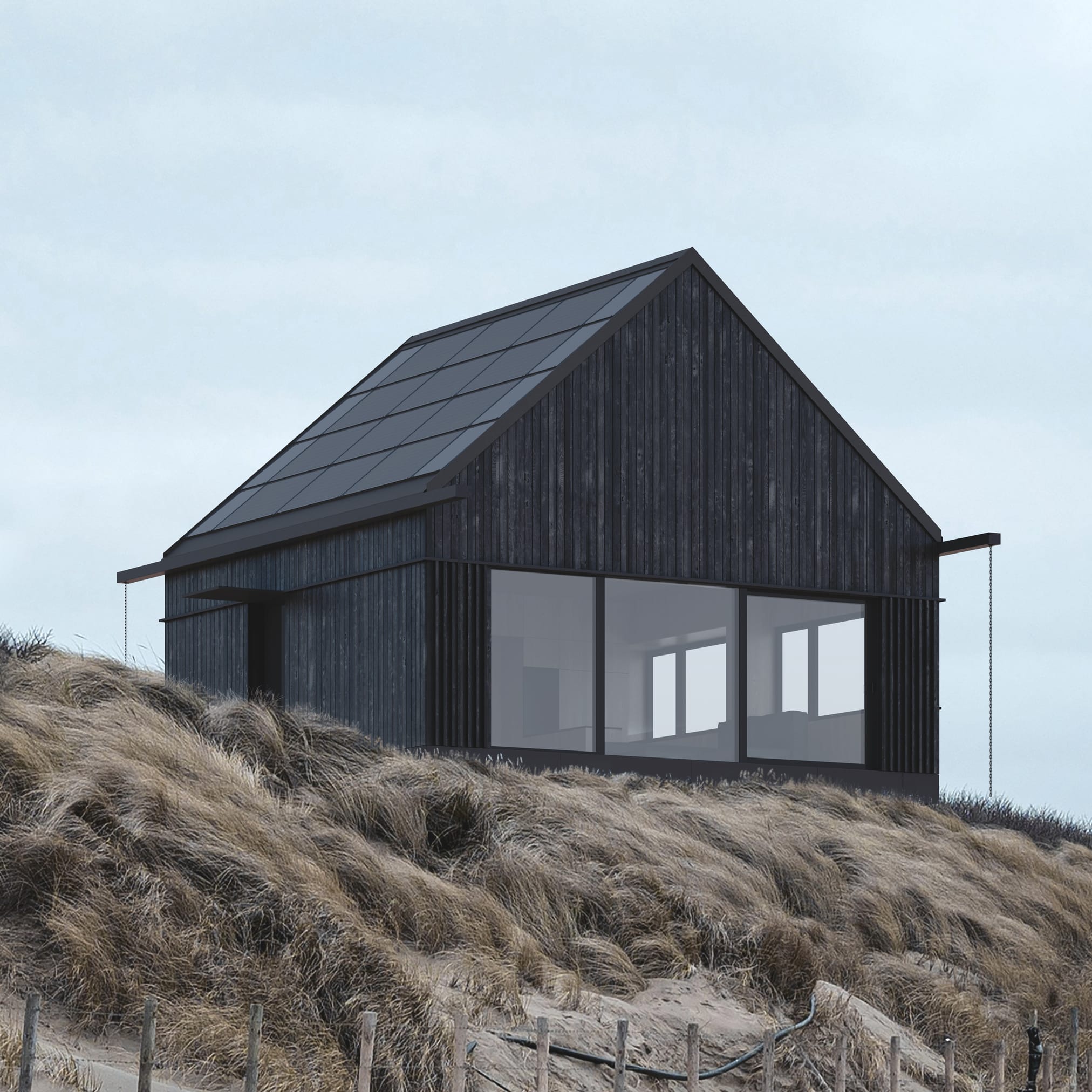 A dark, modern house with a roof entirely covered with photovoltaic panels, standing on a meadow at the foot of forested mountains.