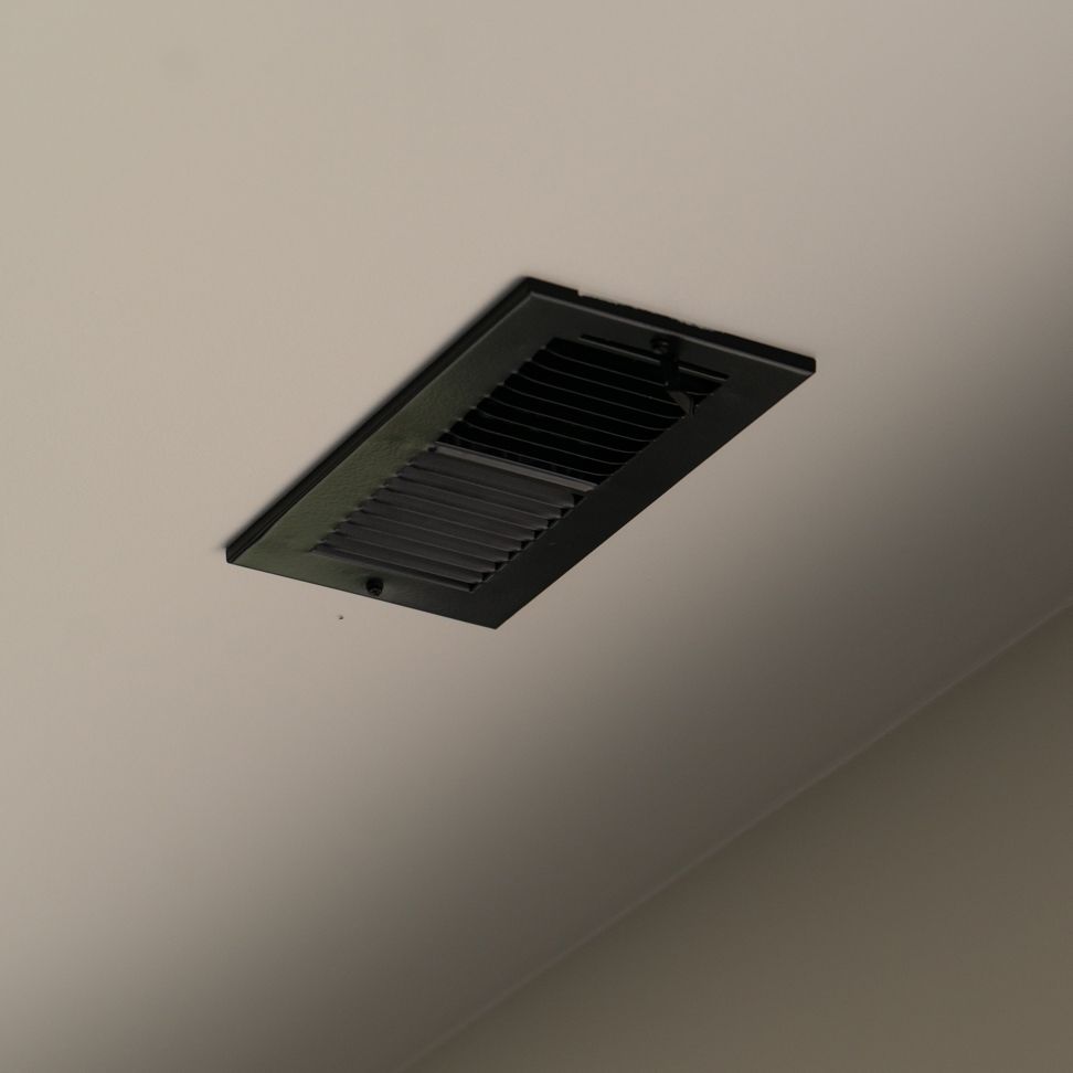 Black, rectangular air vent mounted on a white, smooth ceiling.