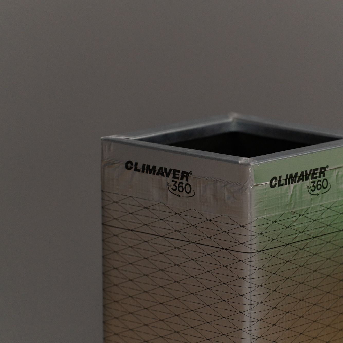 Rectangular, silver air duct standing on a gray background.