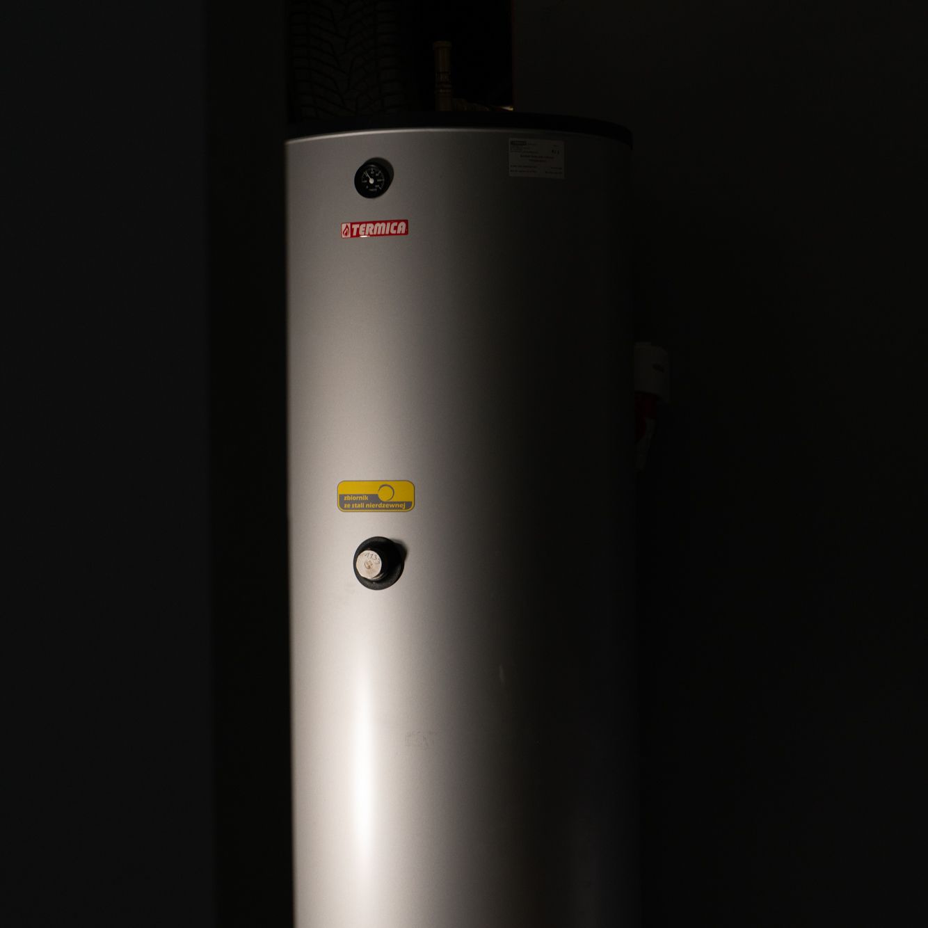 Steel water heater with a cylindrical shape on a black background. There is a gauge and a valve on the water heater.