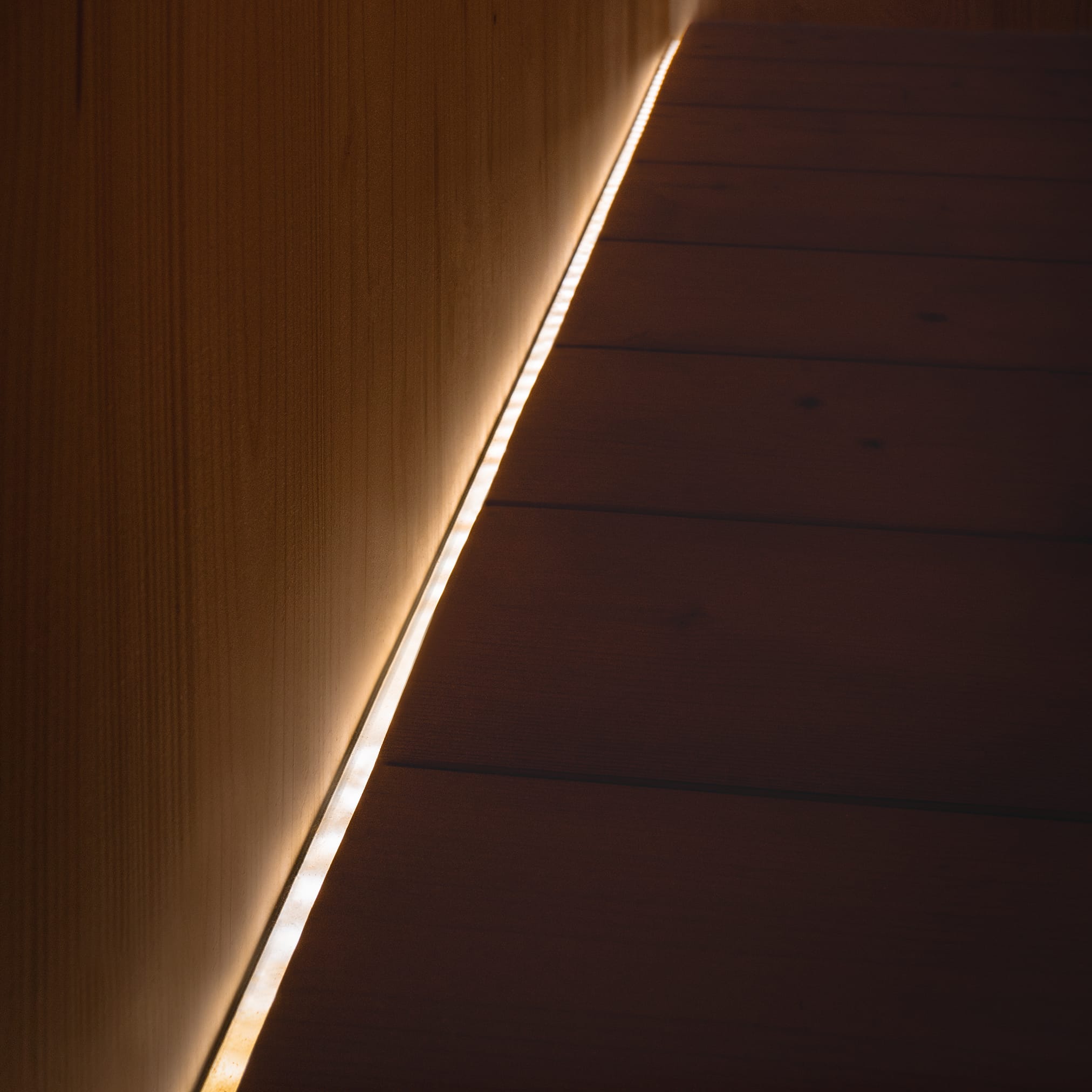 A warm, linear LED lamp built into a wooden structure, running diagonally between a vertical wall and horizontal boards.