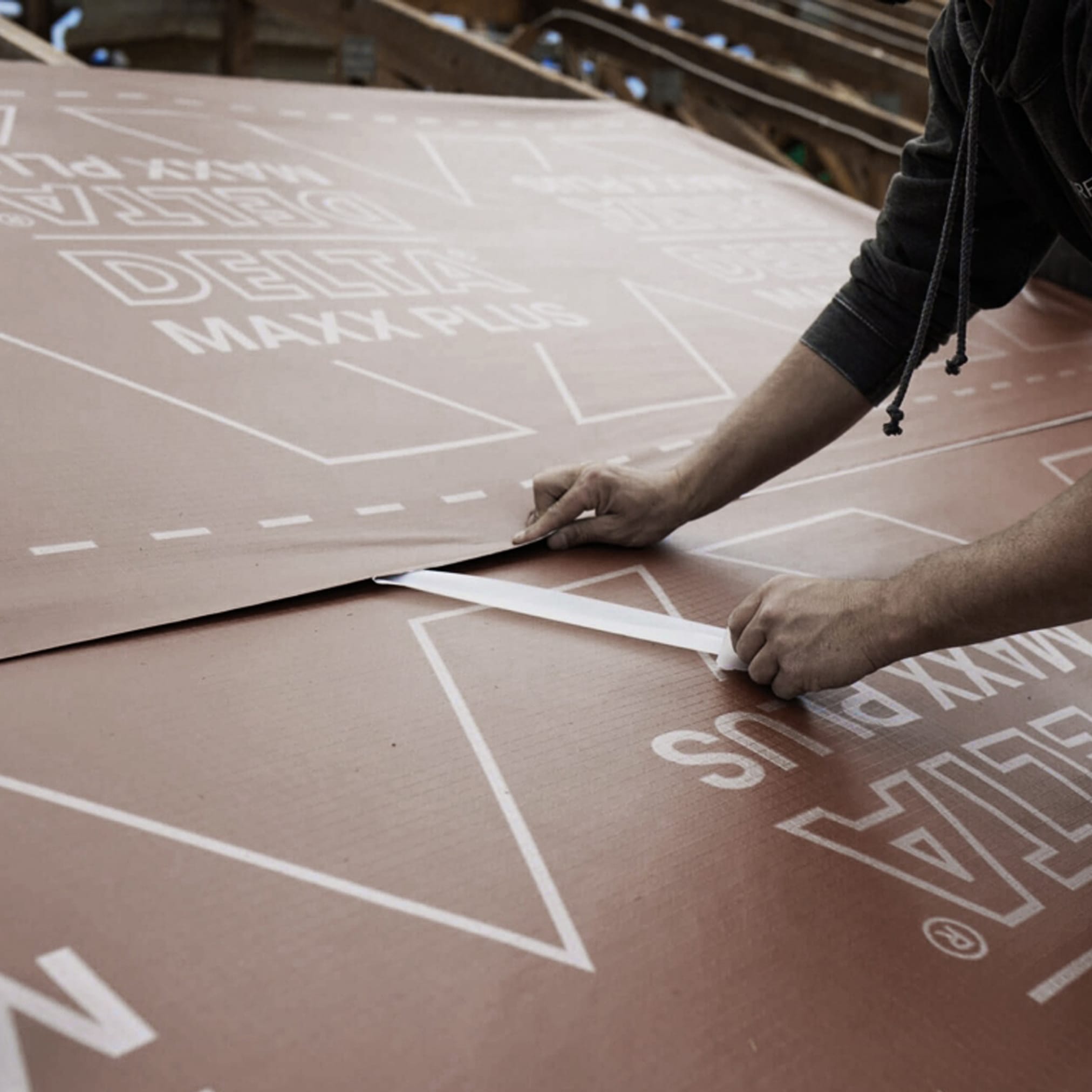 Pracownik montuje duży arkusz brązowej membrany dachowej z białymi napisami.