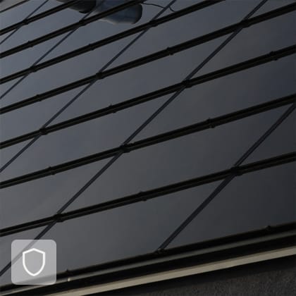 A close-up of a pitched roof covered with dark, integrated photovoltaic panels that form a smooth, uniform surface.
