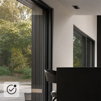 Modern interior with a black high table, a bar stool, and open terrace doors through which lush green vegetation is visible.