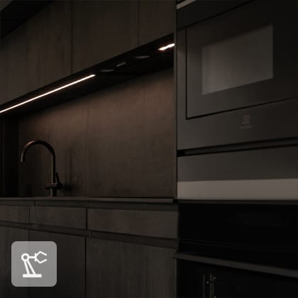 A close-up of a dark, modern kitchen with black cabinets, a black sink, and LED lighting under the upper cabinet.