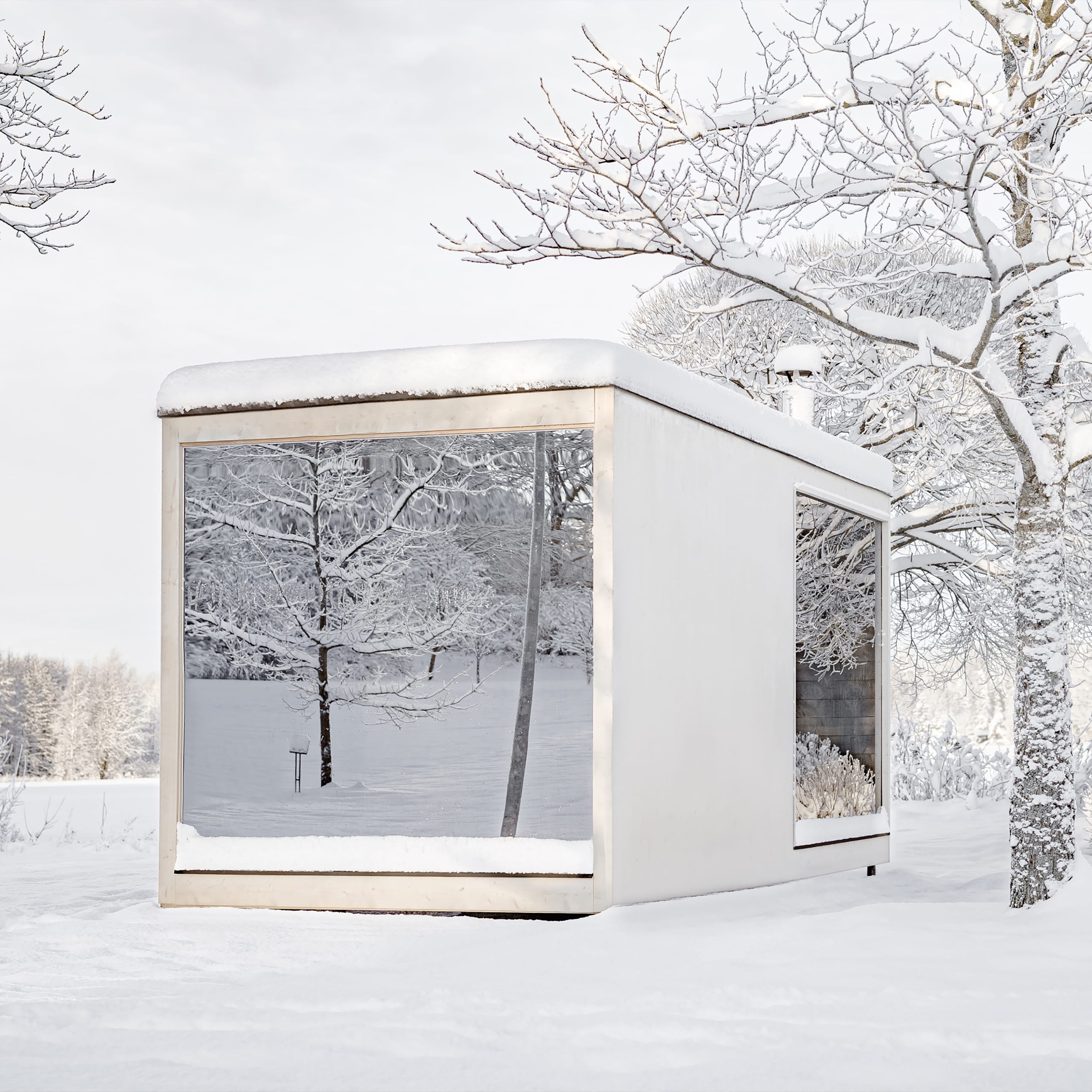 Biała, minimalistyczna kabina z panoramicznymi oknami stoi w ośnieżonym ogrodzie. W szybach odbijają się pokryte śniegiem drzewa.