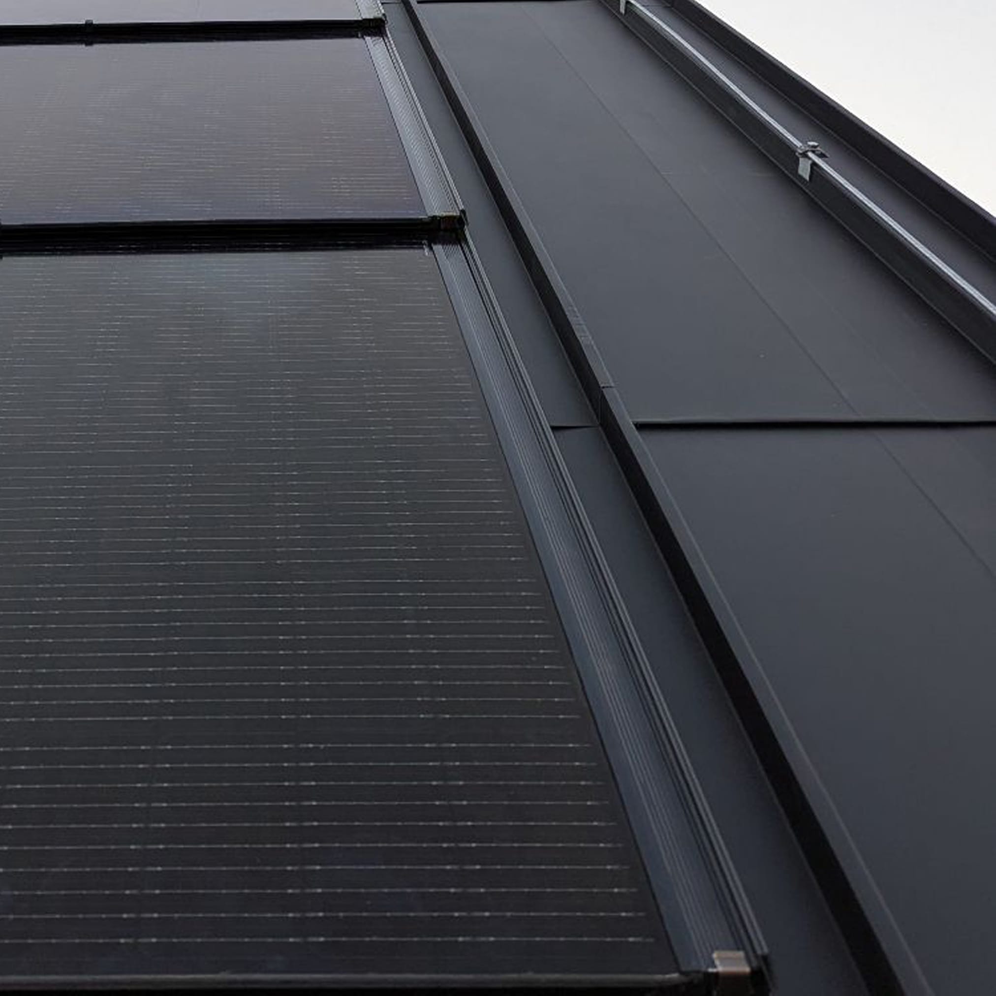 Ujęcie z dołu na ciemny dach budynku, łączący zintegrowane panele fotowoltaiczne z gładką, czarną blachą.