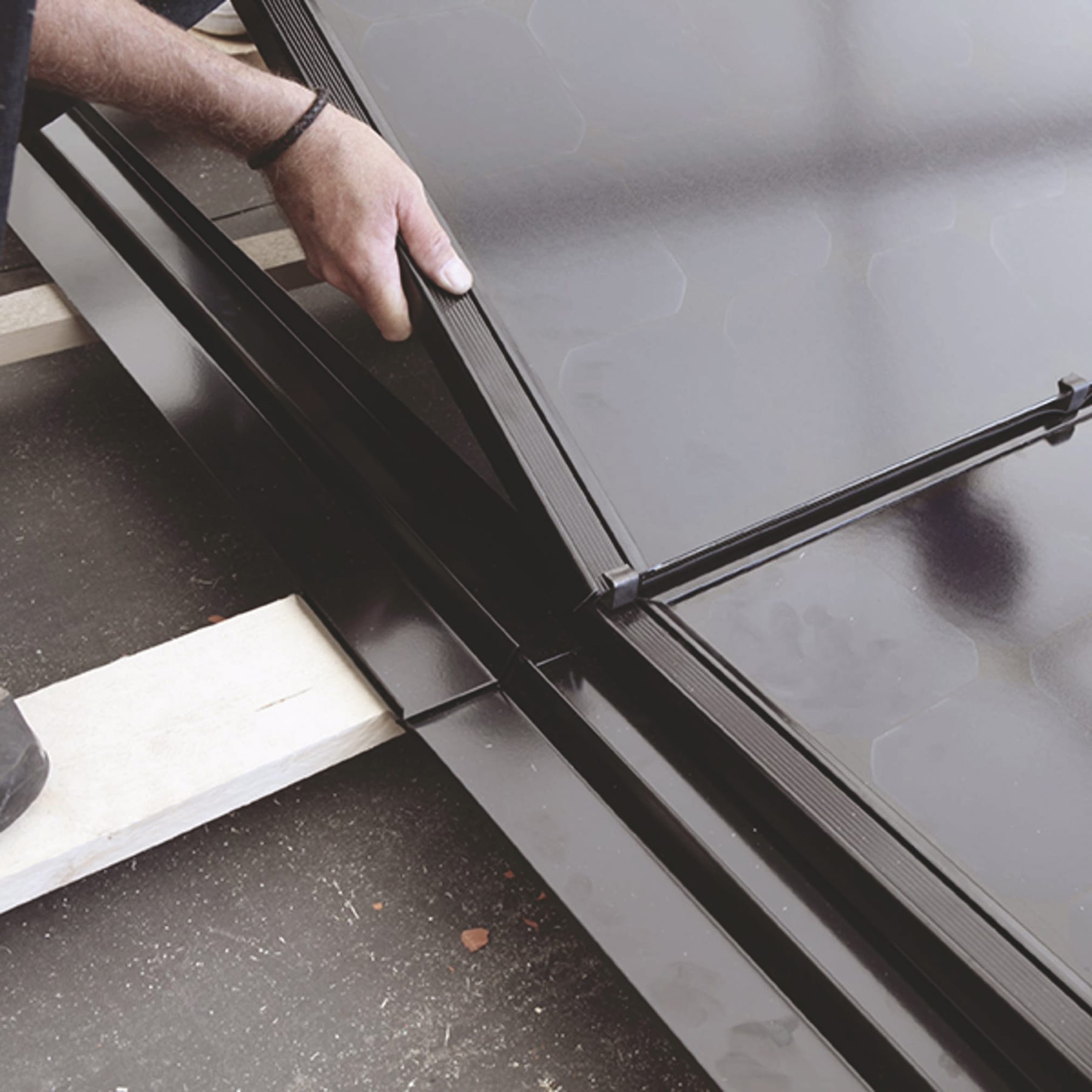 A close-up of a worker's hands inserting a black, smooth photovoltaic panel into a frame.