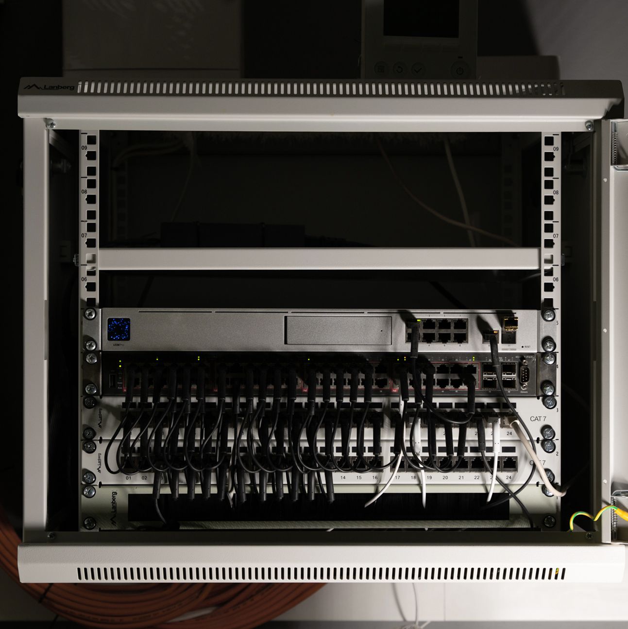 Front of router and other devices mounted in a rack cabinet. Many cables are connected to the devices.