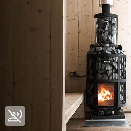 The interior of a sauna finished in light wood, with a black wood-burning stove and a large window with a view of a snowy landscape.